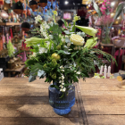 Fris boeket met witte rozen, lelies en groene accenten, stijlvol geschikt in een geribbelde blauwe vaas op een houten tafel.